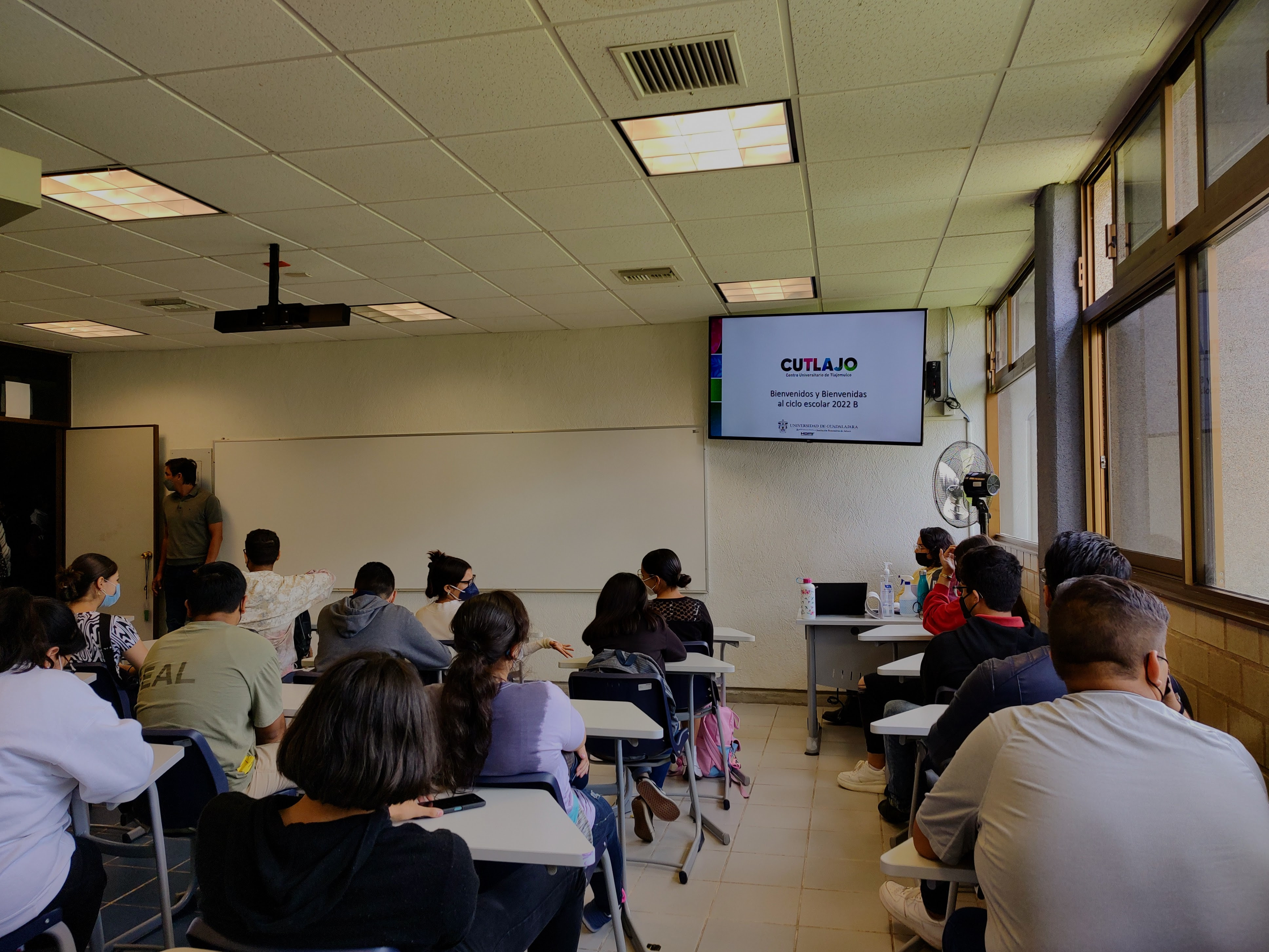 estudiantes en butacas con una televisión al fondo en la que se lee el texto CUTLAJO