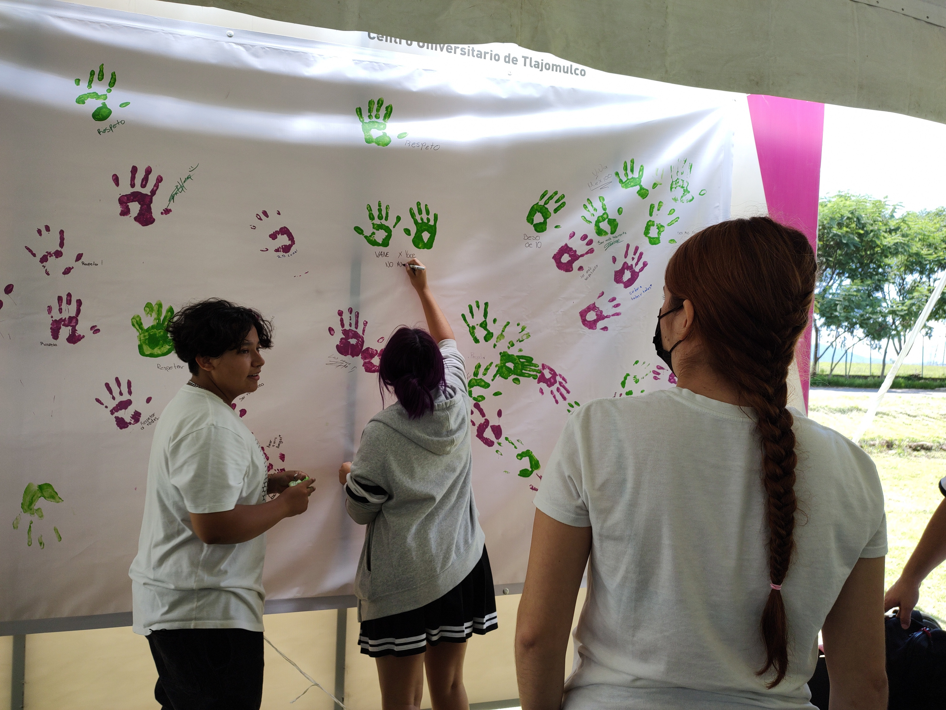 3 personas con camiseta blanca, dos de ellas estan pintando sus manos en una lona blanca.