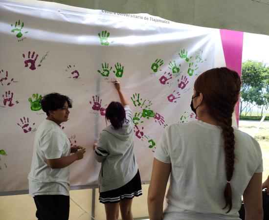 3 personas con camiseta blanca, dos de ellas estan pintando sus manos en una lona blanca.